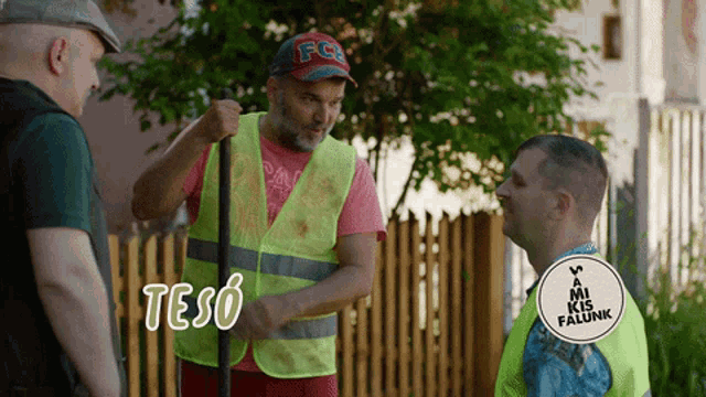 a man wearing a fc hat and a yellow vest talks to another man