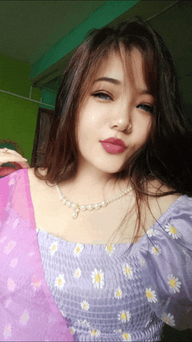 a woman wearing a purple top and a pearl necklace looks at the camera