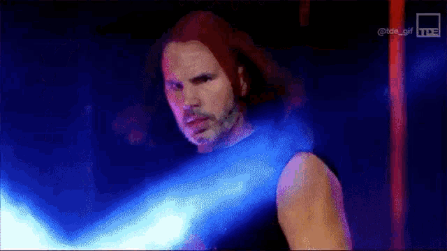 a man with red hair and a beard is holding a blue light sword .
