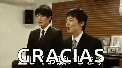 two men in suits and ties are standing next to each other in a room with the word gracias written on the wall .