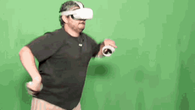 a man wearing a virtual reality headset and holding a controller is dancing on a green screen .