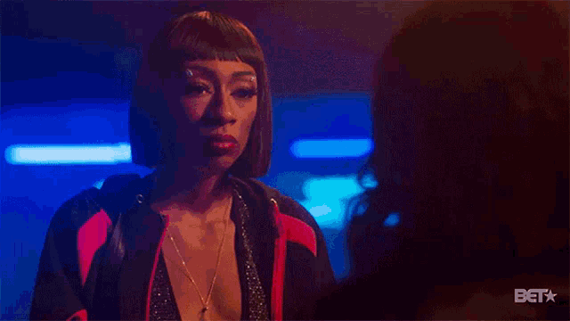 a woman in a red and black jacket is standing next to another woman in a dark room .