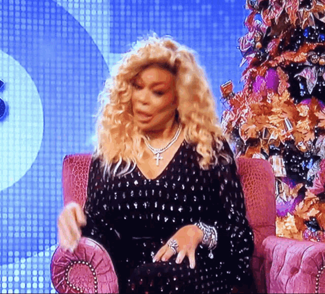 a woman in a black dress is sitting in a chair in front of a christmas tree