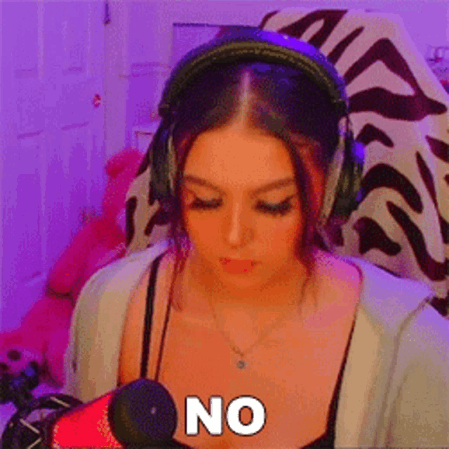 a woman wearing headphones and a necklace is sitting in front of a microphone and saying no .