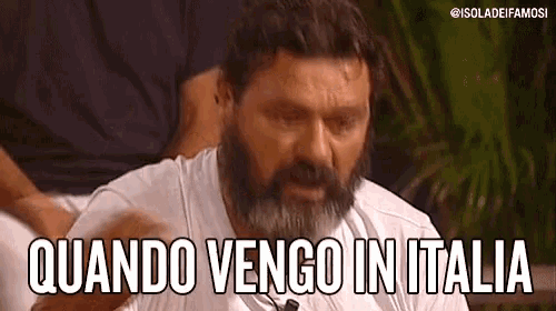 a man with a beard and a white shirt is sitting down and saying quando vengo in italia .