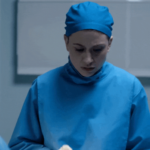 a female surgeon wearing a blue cap and gown looks down