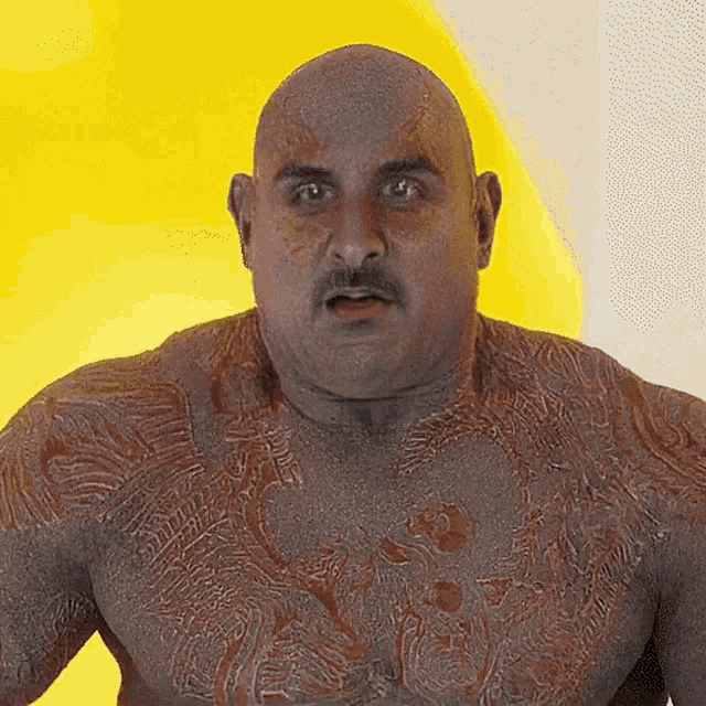 a bald man with a mustache and a tattoo on his chest looks surprised