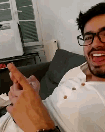 a man wearing glasses and a white shirt is sitting on a couch and sticking his tongue out