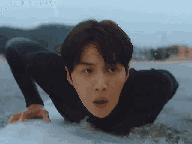 a man in a wetsuit is crawling on a surfboard in the ocean .