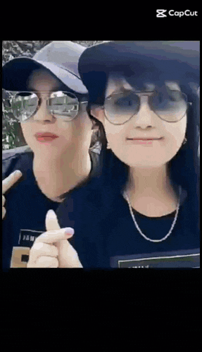two women wearing hats and sunglasses are giving a thumbs up .