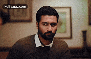 a man with a beard is sitting at a table in a room looking at the camera .