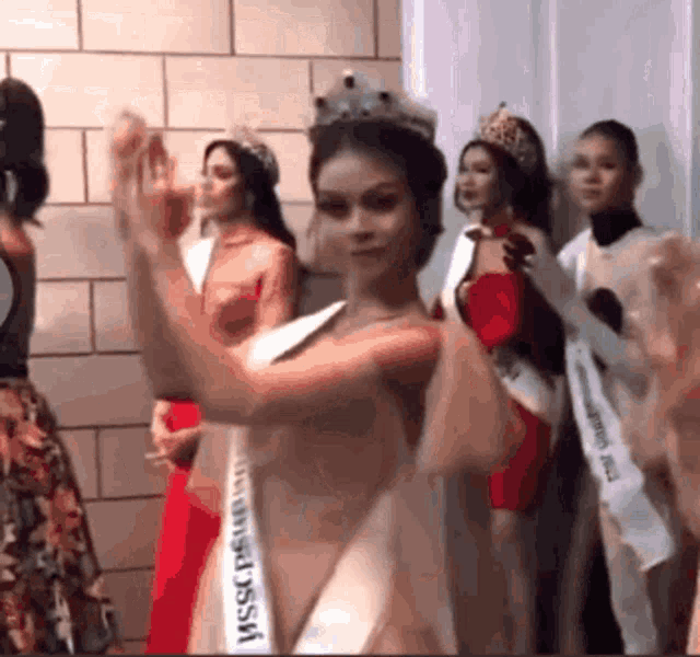 a group of women are standing in a room and one of them is wearing a sash that says ' miss universe ' on it