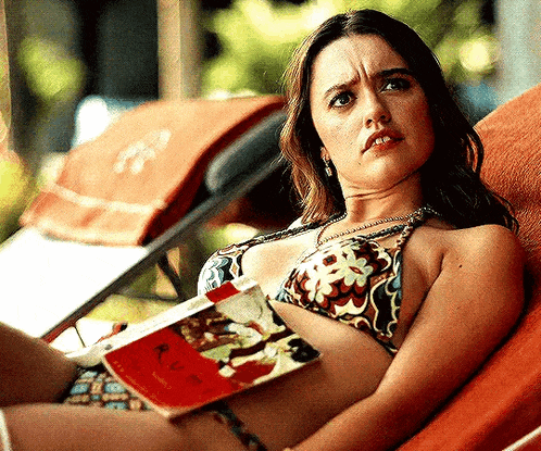 a woman in a bikini is laying on a lounge chair reading a book .