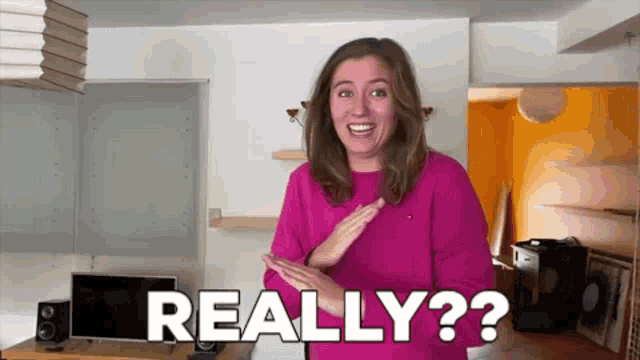 a woman in a pink sweater is making a funny face and saying really ? in a living room .