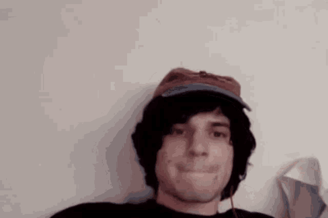 a man wearing a hat and headphones is laying on a bed and making a funny face .