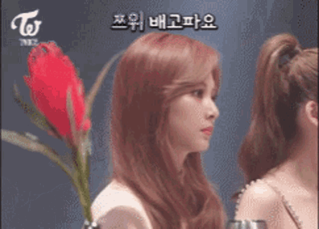 a woman with red hair is holding a red flower in front of a sign that says twice