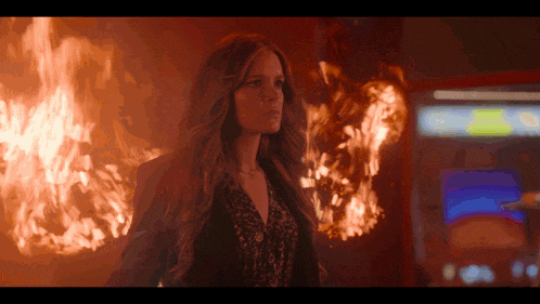 a woman is standing in front of a fire with a game machine in the background
