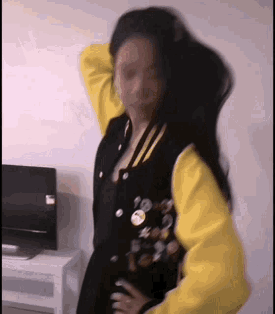 a woman in a black and yellow jacket is standing in front of a tv .