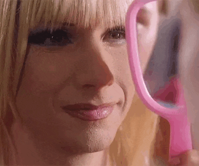 a woman is holding a pink mirror in front of her face .