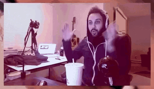 a man with a beard wearing headphones holds a cup of soda