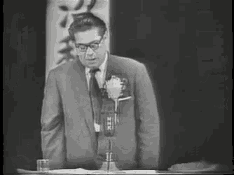 a man in a suit and tie is standing in front of a microphone in a black and white photo .