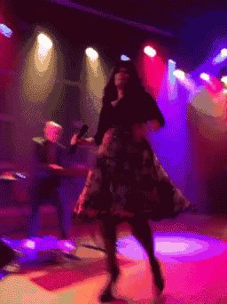 a pixelated image of a woman dancing with a man playing drums in the background