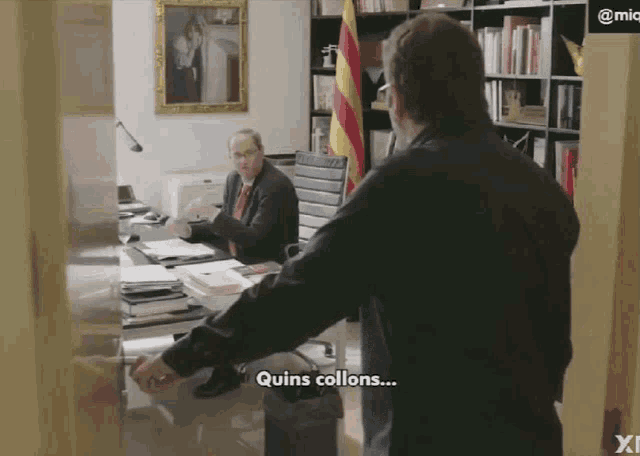 a man standing in front of a desk with quins collons written on the screen