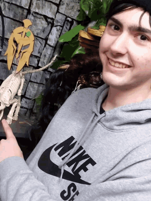 a man wearing a gray nike sweatshirt points to a skeleton