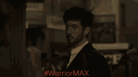 a man in a suit stands in front of a sign that says " warrior max "