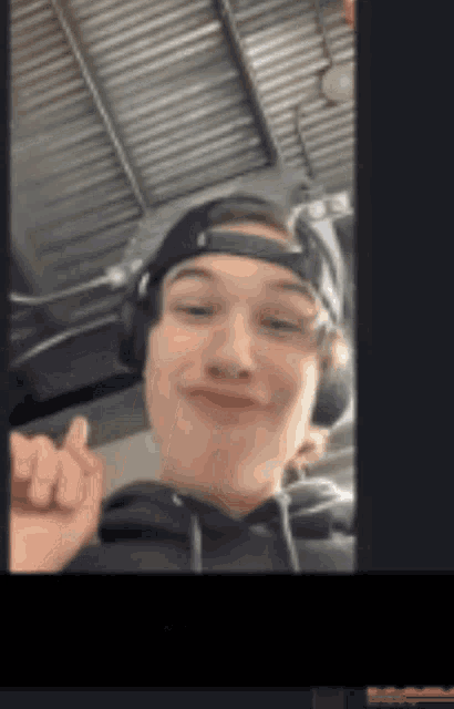 a young man wearing headphones and a hat is giving a thumbs up .