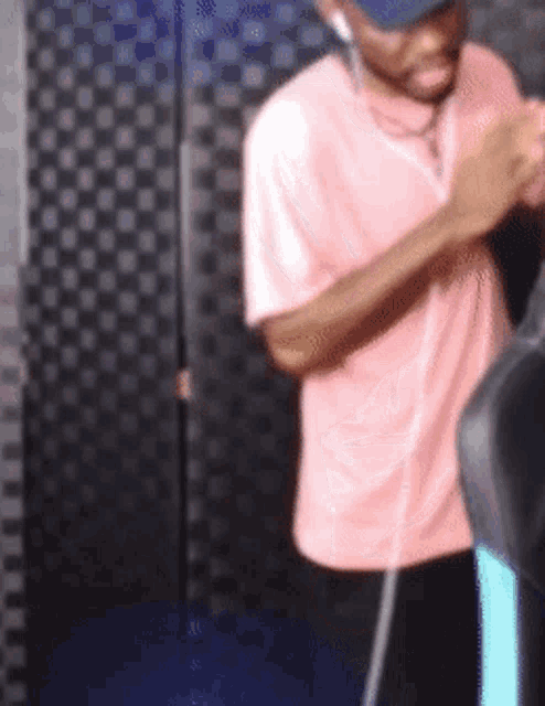 a man wearing a pink shirt and a baseball cap is standing in front of a checkered wall
