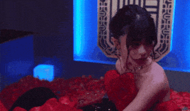 a woman in a red dress sits on a bed of red roses
