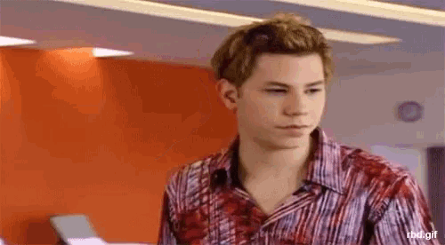 a young man wearing a red and white striped shirt is standing in front of an orange wall .