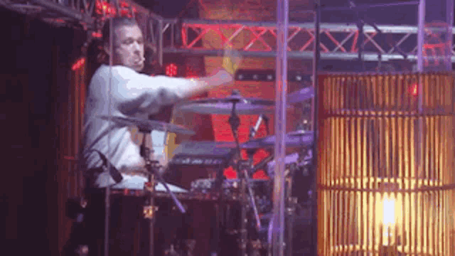 a man playing drums in a dark room with a lamp in the background