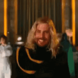 a man with long blonde hair and a beard is smiling and holding his head .