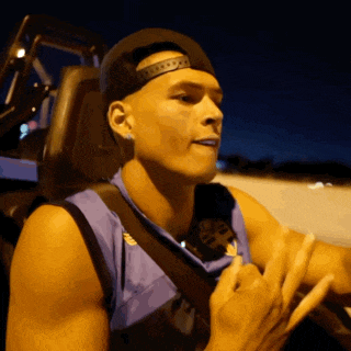 a man wearing a hat and a purple tank top is sitting in a vehicle