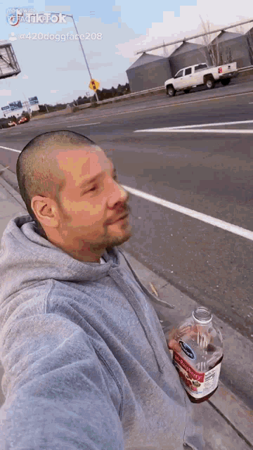 a man is taking a selfie while holding a bottle of soda on the side of the road .