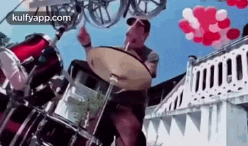 a man is playing drums in front of balloons and a building .