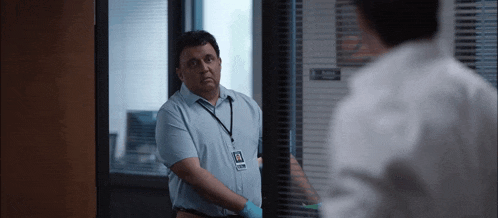 a man in a blue shirt and tie is standing in front of a window in an office .
