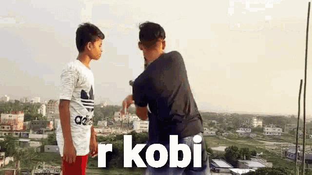 two young men are standing next to each other on top of a building and talking to each other .