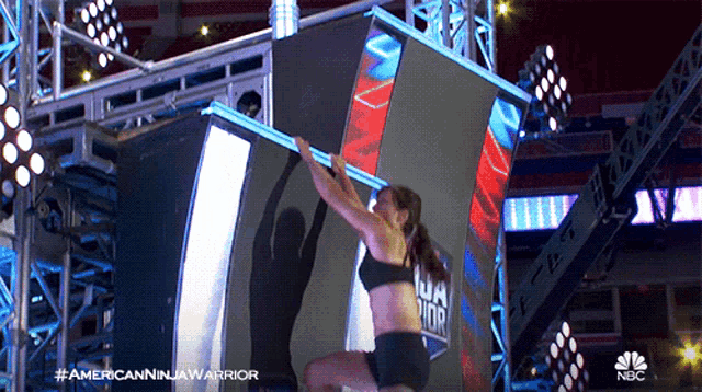 a woman is doing a pull up in front of a large screen that says americanninjawarrior