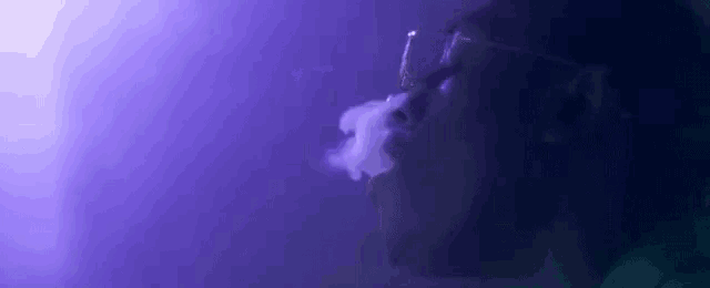 a man is smoking an electronic cigarette in a dark room with purple lights .