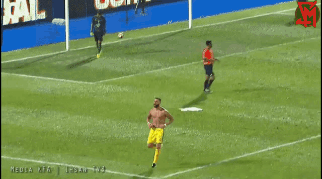 a man without a shirt is running on a soccer field in front of a goal