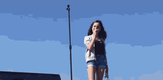a woman is singing into a microphone while standing in front of a blue sky