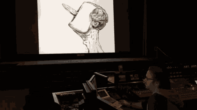 a man sitting in front of a large screen with a drawing of a man on it