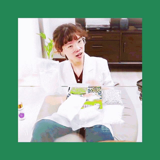 a woman wearing glasses and a lab coat is sitting on a couch holding a bag of beans