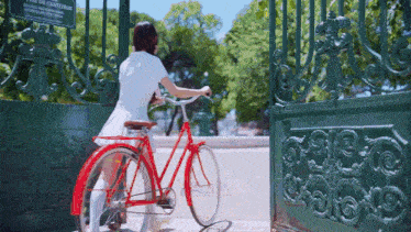 a woman in a white dress is riding a red bicycle through a gate