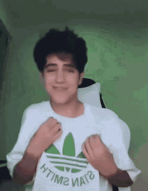 a young man wearing a white adidas t-shirt is making a funny face