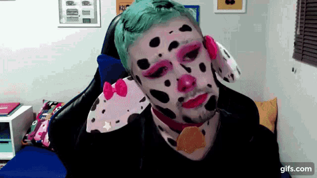 a man with green hair and dalmatian makeup is sitting in a chair ..