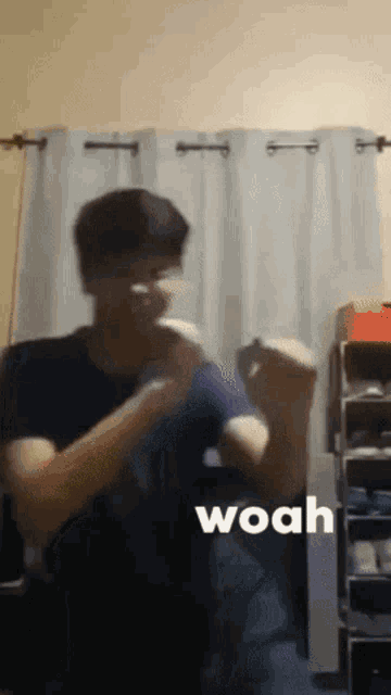 a man in a blue shirt is dancing in front of a white curtain with the word woah on the bottom